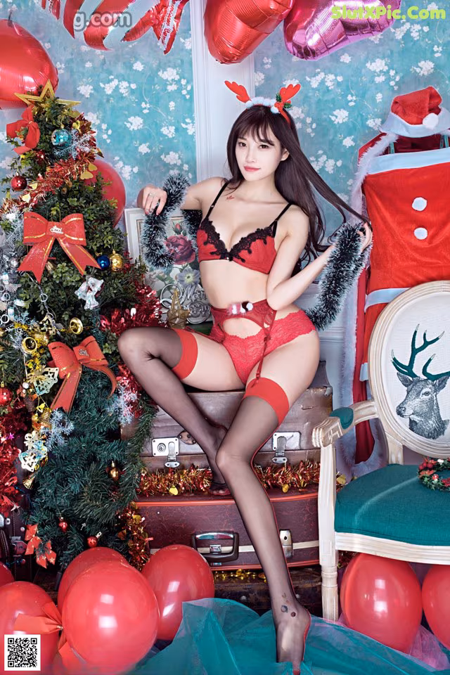 A woman in a red lingerie sitting on a chair next to a Christmas tree.