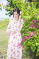 A pregnant woman standing in front of a bush of flowers.