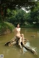 A naked woman sitting on a log in the water.