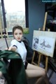 A woman sitting in front of a painting on a easel.