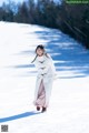 A woman walking in the snow wearing a white coat.