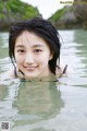 A young woman in the water smiling at the camera.