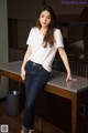 A woman in a white shirt and jeans leaning on a table.