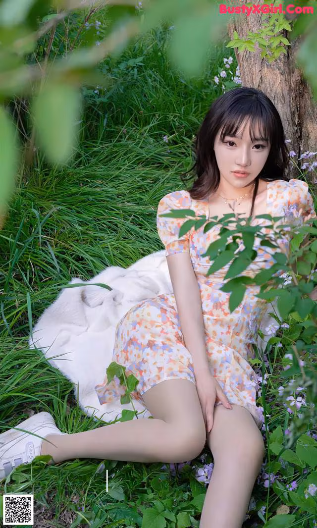 A woman in a floral dress sitting in the grass.